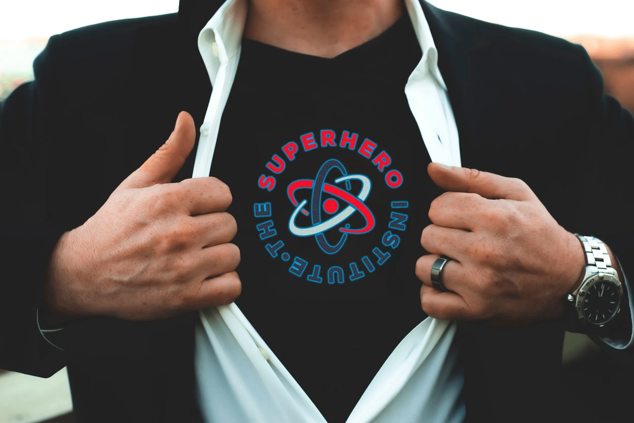 A man in a dark jacket pulling open his shirt to reveal the Superhero Institute logo on his chest